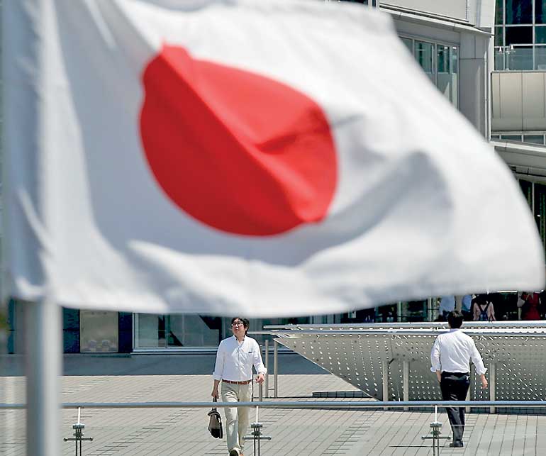 Businessmen walk behind a Japanese national flag at a convention centre in Tokyo