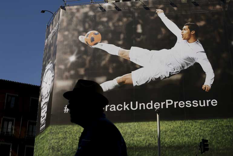 A man walks past a billboard displaying an image of Real Madrid's soccer player Cristiano Ronaldo kicking a ball in Madrid