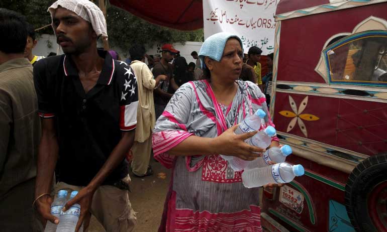 Volunteers cover their heads with water-soaked towels, to beat the heat, while distributing water bottles, outside Jinnah Postgraduate Medical Centre in Karachi