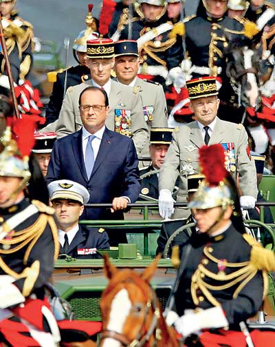 French President Francois Hollande stands at attention in the command car as he reviews the troops while descending from the Champs Elysees at the start of the traditional Bastille Day military parade in Paris