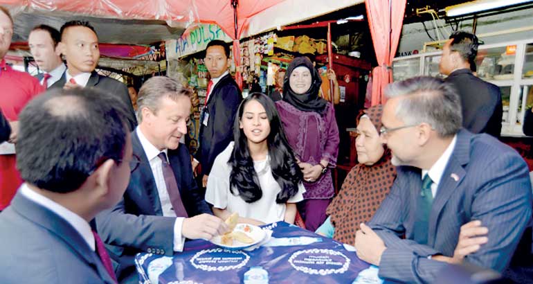 British Prime Minister David Cameron is accompanied by Indonesian entertainer Maudy Ayunda after ordering fried bananas at a street food stall after his visit to Sunda Kelapa Mosque in Jakarta