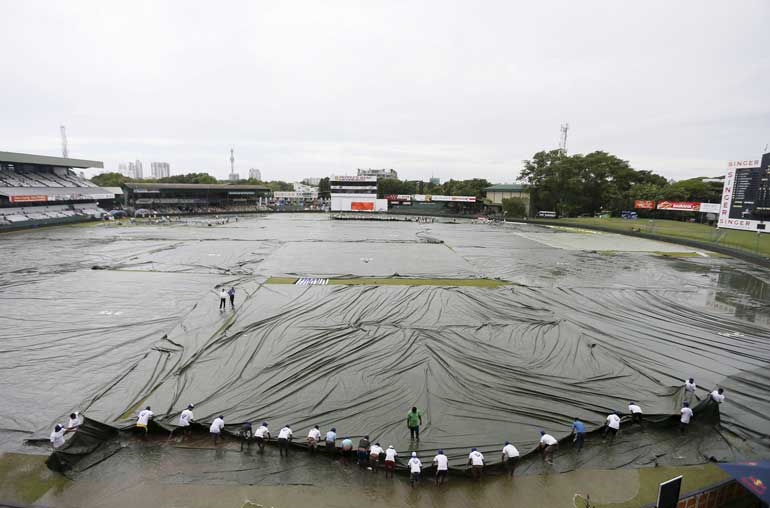 Ground workers pull the covers to cover the ground as the match was stopped due to rain, on the first day of third and final test cricket match between India and Sri Lanka in Colombo