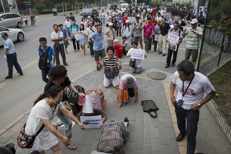 People whose relatives were aboard Malaysia Airlines flight MH370 kneel and cry in front of the media near the Malaysian embassy in Beijing after protesting relatives scuffled briefly with police who stopped them from entering a road leading to the embass