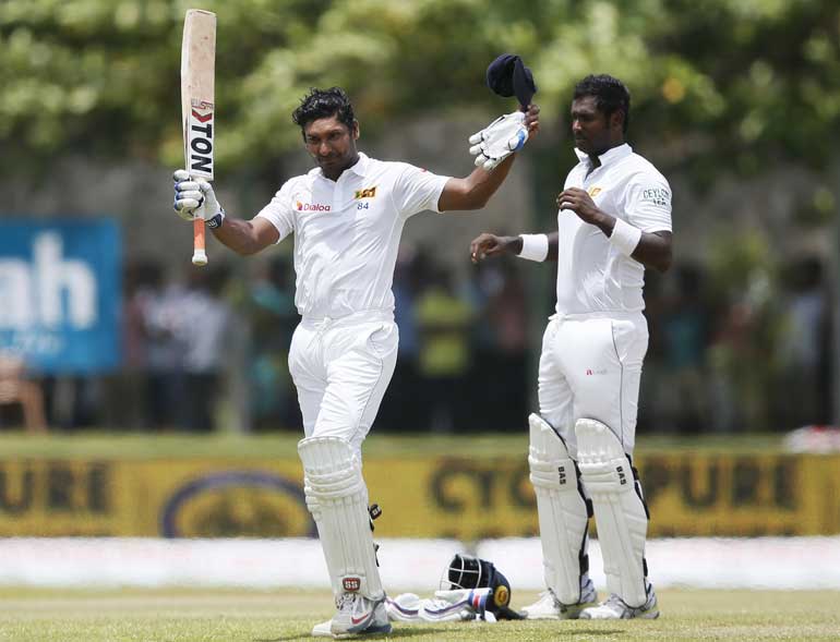 Sri Lanka's Sangakkara raises his bat and cap for fans as he walks off the field after his dismissal by India's Ashwin next to Sri Lanka's captain Mathews during the third day of their first test cricket match in Galle
