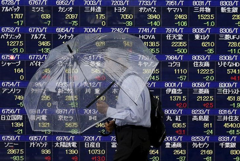 A man holding an umbrella walks in front of an electronic stock quotation board outside a brokerage in Tokyo