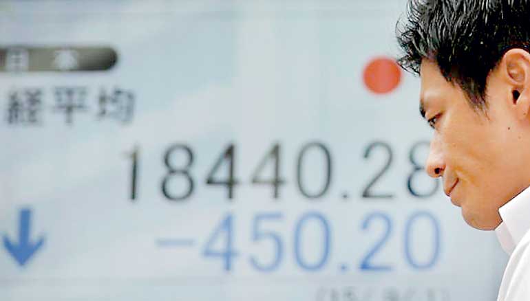 Man walks past an electronic board showing Japan's Nikkei average outside a brokerage in Tokyo