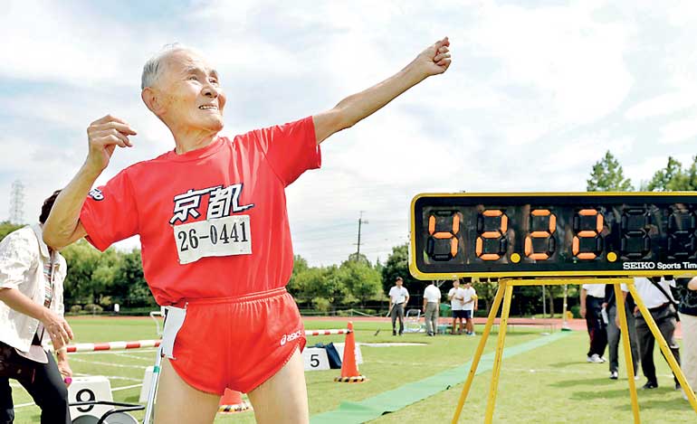 Japanese Hidekichi Miyazaki poses like Jamaica's Usain Bolt in front of an electric board showing his 100-metre record time of 42.22 seconds at an athletic field in Kyoto