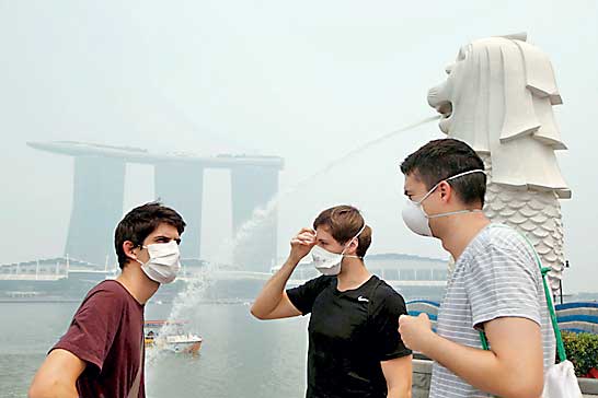 Tourists wearing masks visit the Merlion Park shrouded by haze in Singapore