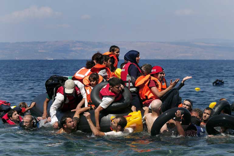 Syrian and Afghan refugees are seen on and around a dinghy that deflated some 100m away before reaching the Greek island of Lesbos