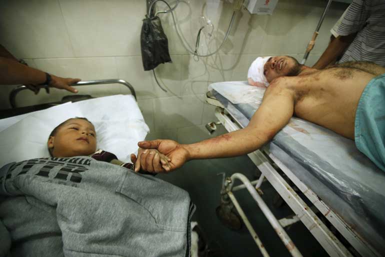 A wounded Palestinian boy and his father hold hands at a hospital after their house was brought down by an Israeli air strike in Gaza