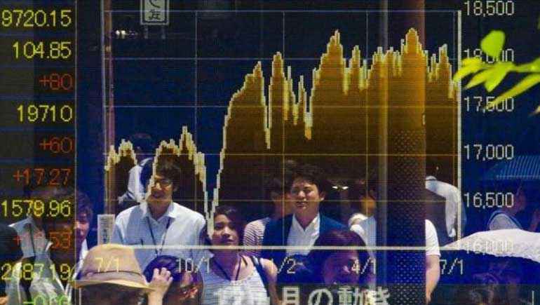 People are reflected in board displaying market indices in Tokyo