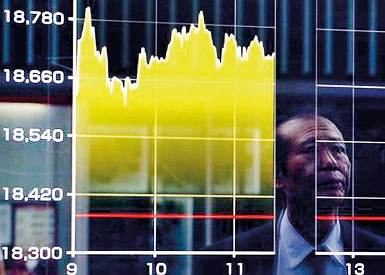 A pedestrian is reflected on an electronic board showing the graph of the recent fluctuations of the Japan's Nikkei average outside a brokerage in Tokyo