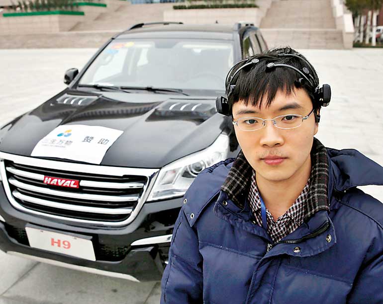 Researcher Zhang Zhao wearing a brain signal-reading equipment poses with a vehicle which can be controlled with his brain wave, during a demonstration at Nankai University in Tianjin