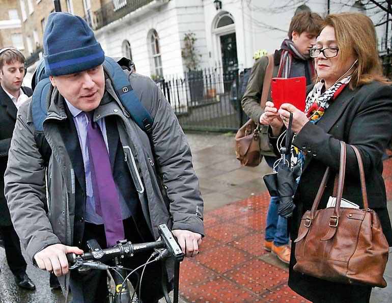 London Mayor Boris Johnson cycles off after speaking to the media in front of his home in London